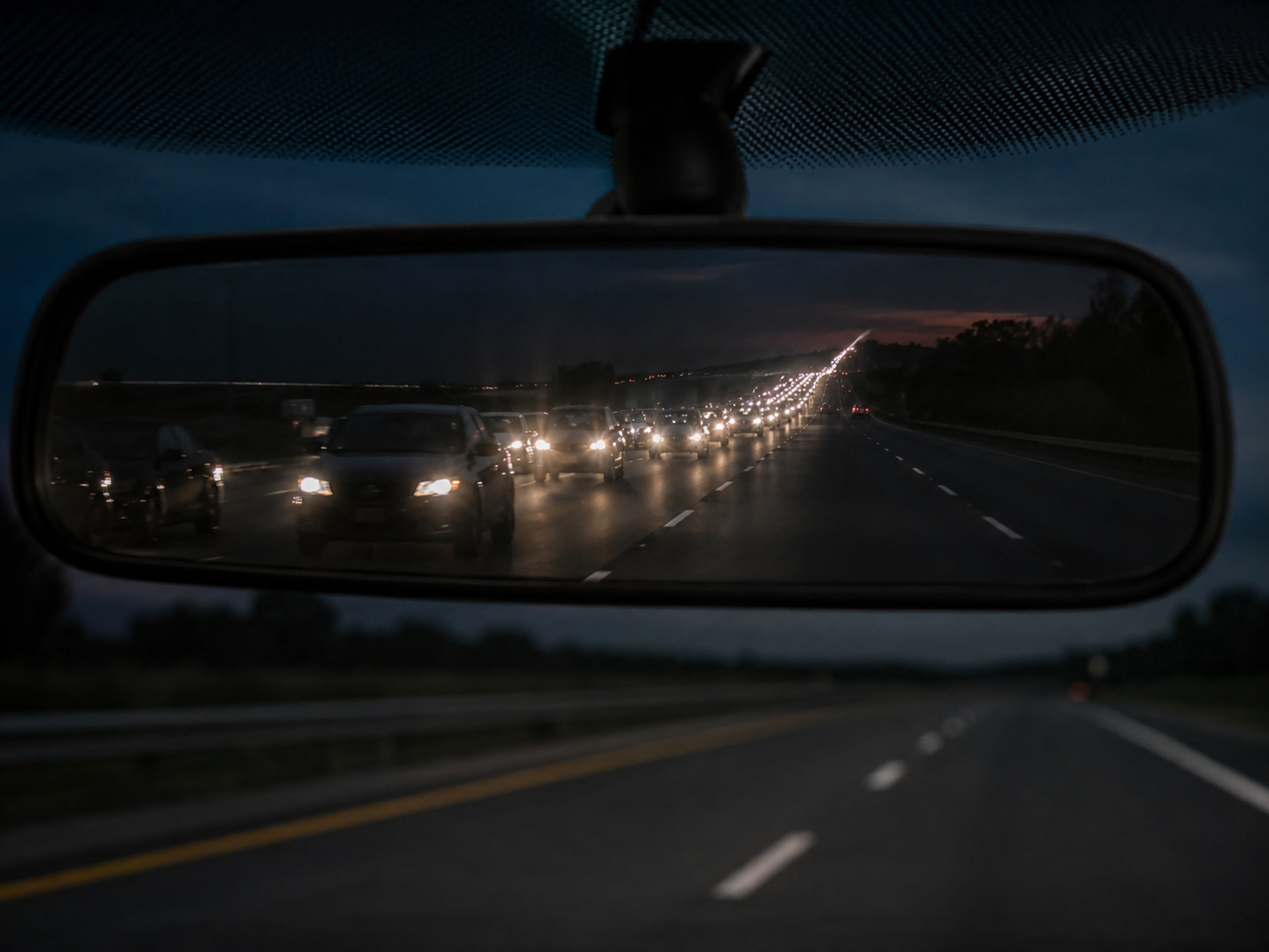 Rétroviseur intérieur reflétant une longue file de phares sur autoroute de nuit